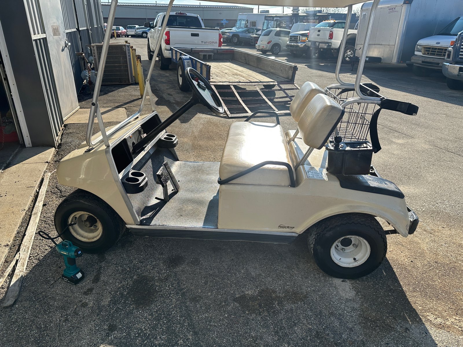 Side view of the tan Club Car outside the shop with a cordless inflator connected to the front tire