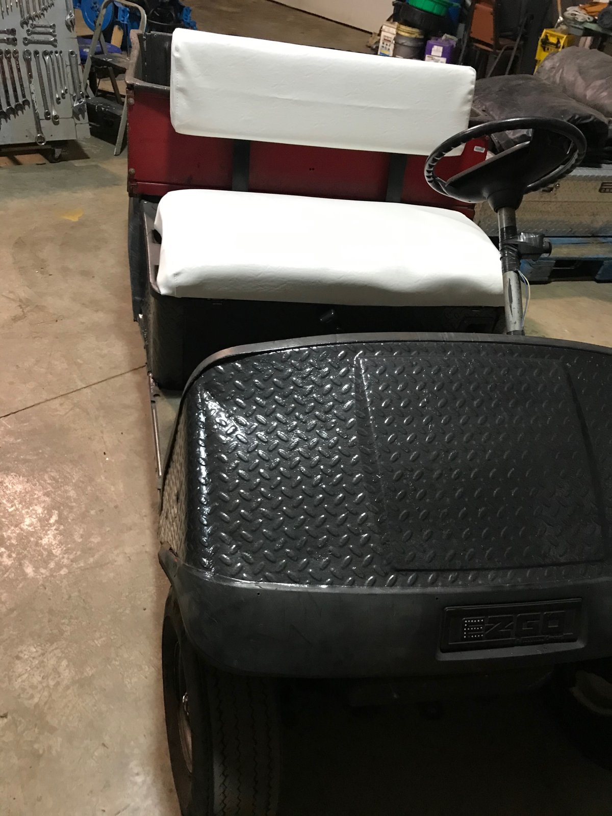 Front view of the EZGO Workhorse in the shop with a newly recovered white seat and a diamond-plate steel front body