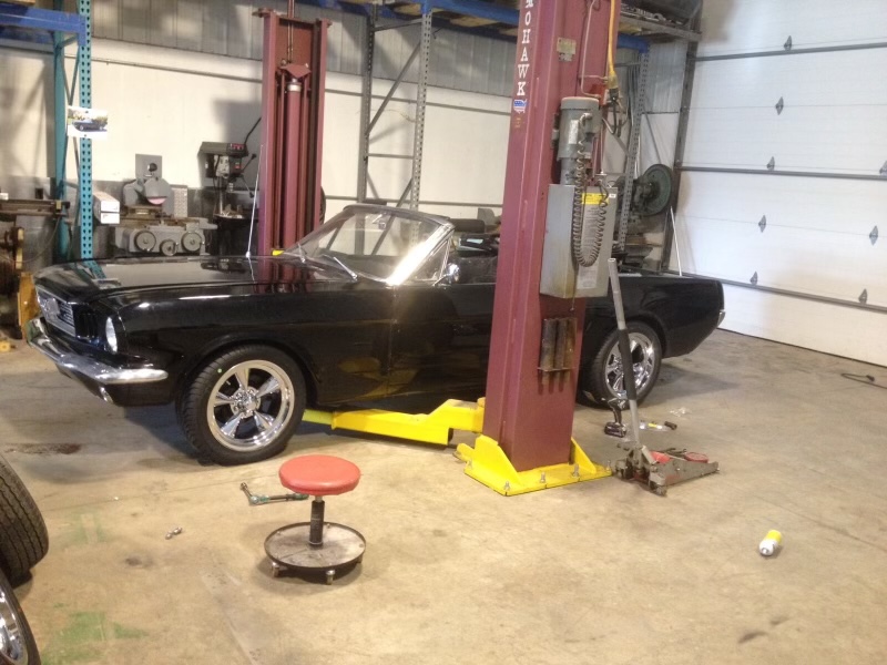 The nearly completed black Mustang convertible on Eric's shop lift with its new chrome wheels installed