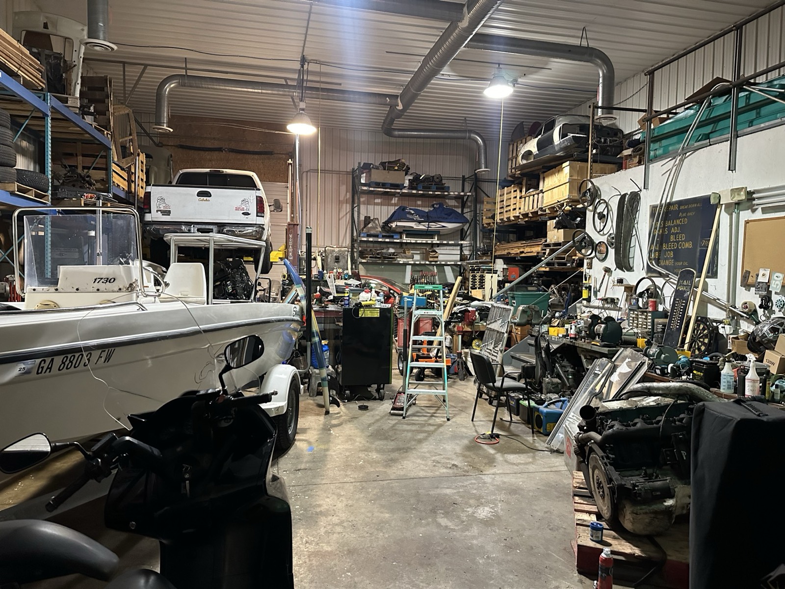 A recent view inside Eric's shop with an F-250 on the lift, a SeaSwirl boat, engines, tools, and pallet racking