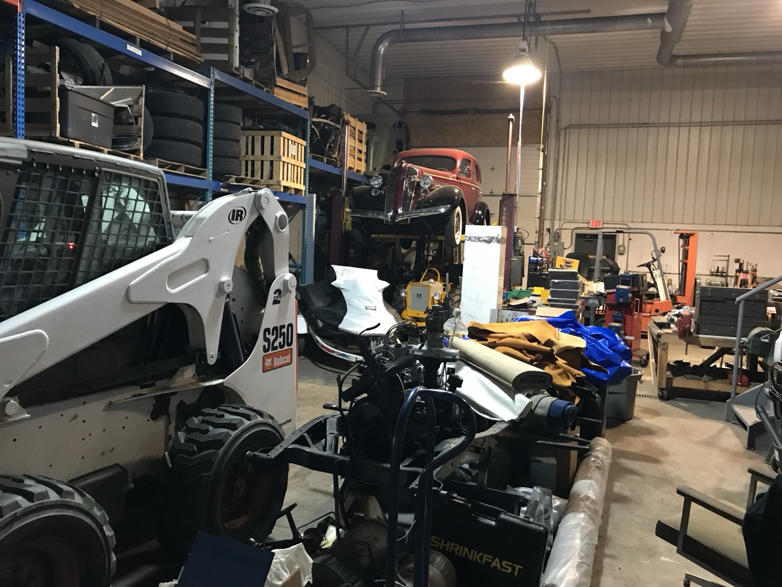 Eric's shop filled with projects, including a Bobcat, a 1936 Graham on the lift, and a Cub tractor beneath it